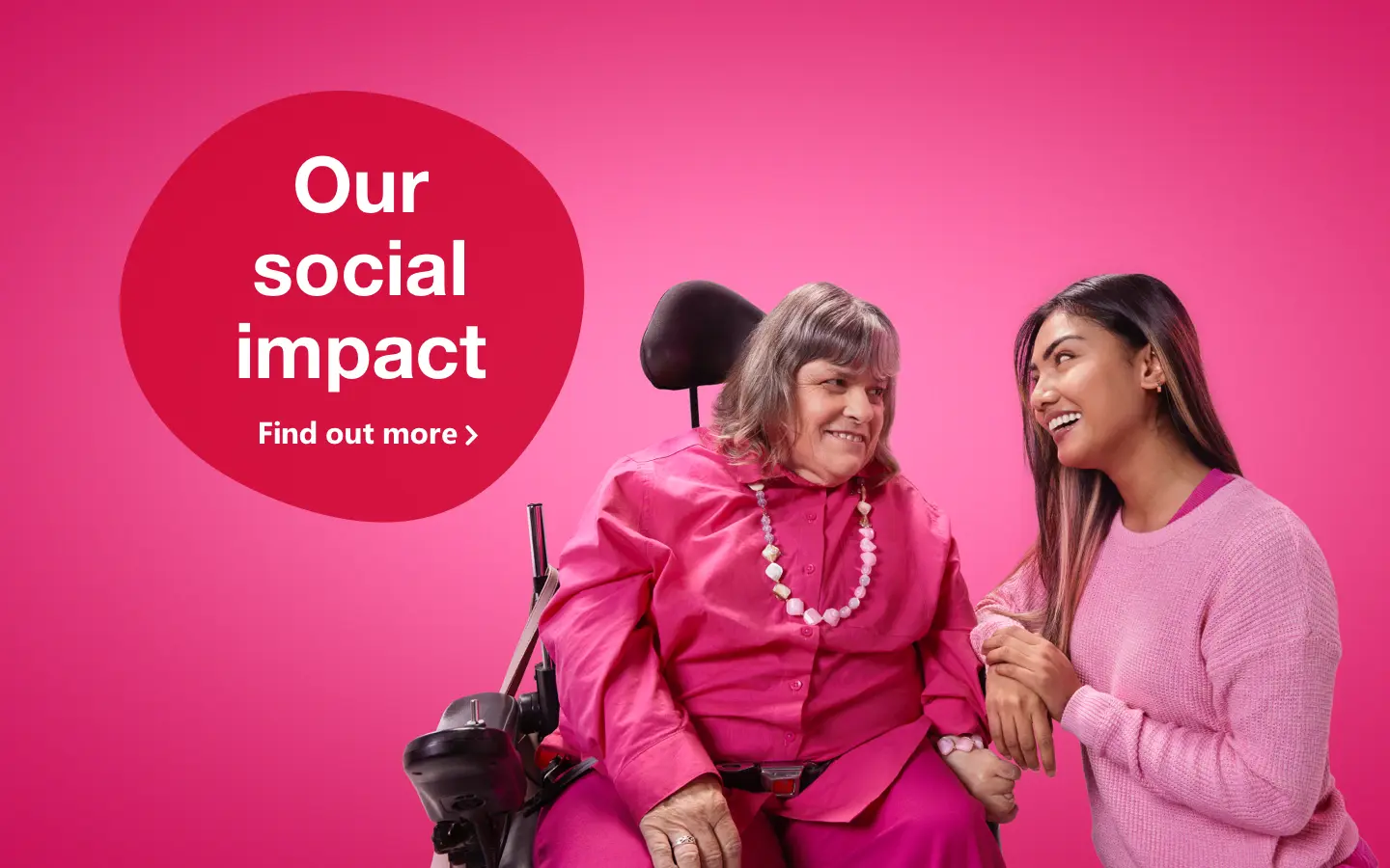 Two women dressed in pink staring at each other smiling, one is in a wheelchair