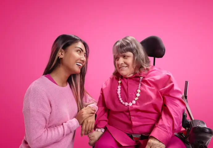 Two women dressed in pink staring at each other smiling, one is in a wheelchair