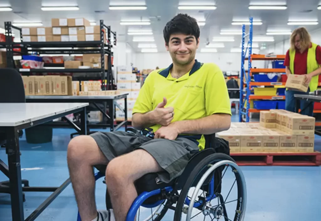 Man in yellow high-vis in warehouse, in a wheelchair