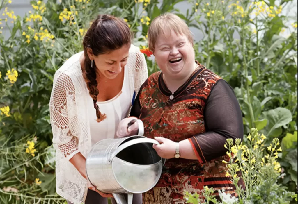 Two people in a garden with a watering can smiling