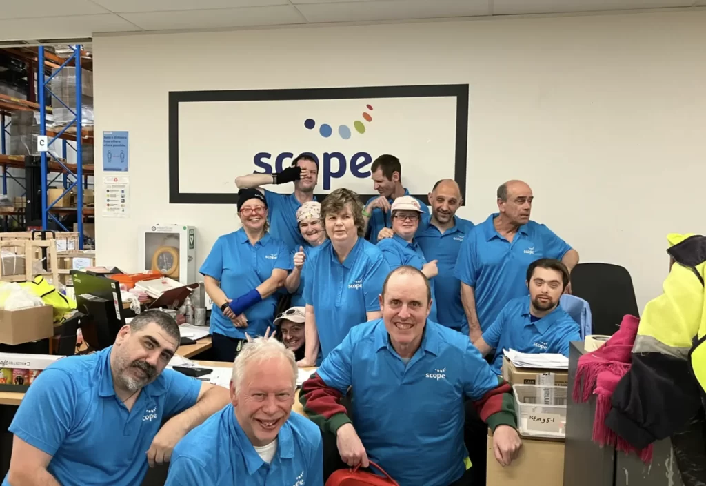 The scope team in blue shirts in front of the logo in an office environment