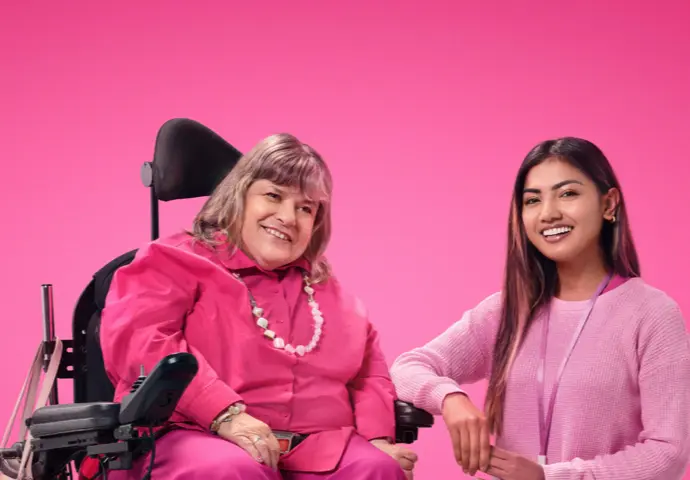 Two women dressed in pink staring at each other smiling, one is in a wheelchair